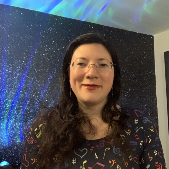 A selfie of me wearing a popsy dress talking visibility and my book, with galaxy background and aurora borealis lighting.