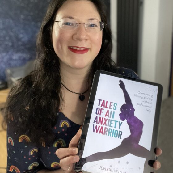 A selfie of me in a rainbow dress. holding a digital copy of my book's cover, looking excited! Tales of an Anxiety Warrior