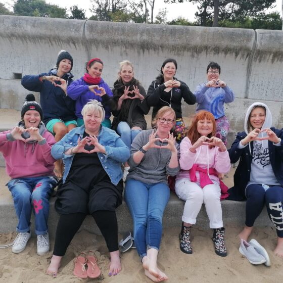 A group picutre on colwyn bay beach, everyone is doing the heart sign with their hands and looking happy!