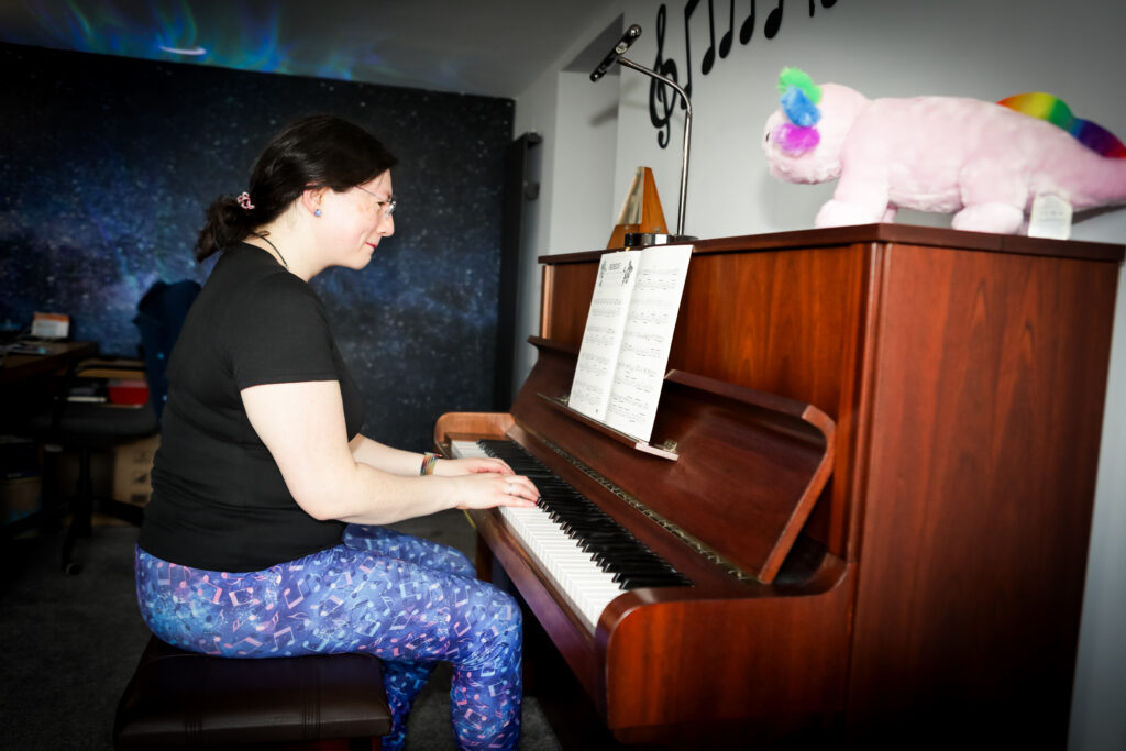 Welcome 13 Jen is playing her piano, there's splatoon music on the stand. You can see a rainbow axolotl in the foreground, and the galaxy wallpaper in the background.