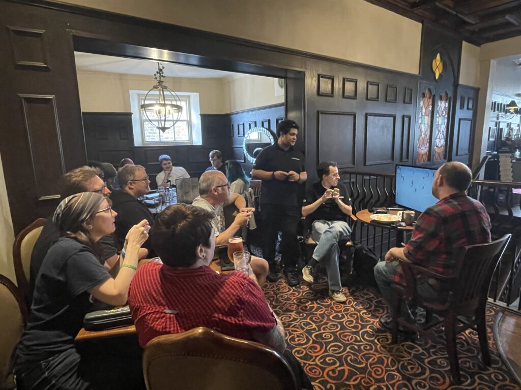 a group photo of a selection of people playing Nintendo Switch on a TV screen. our Plan B was chilling in the local Wetherspoons for the day.