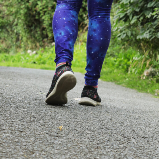Jen is walking down a path in her galaxy themed leggings and trainers.