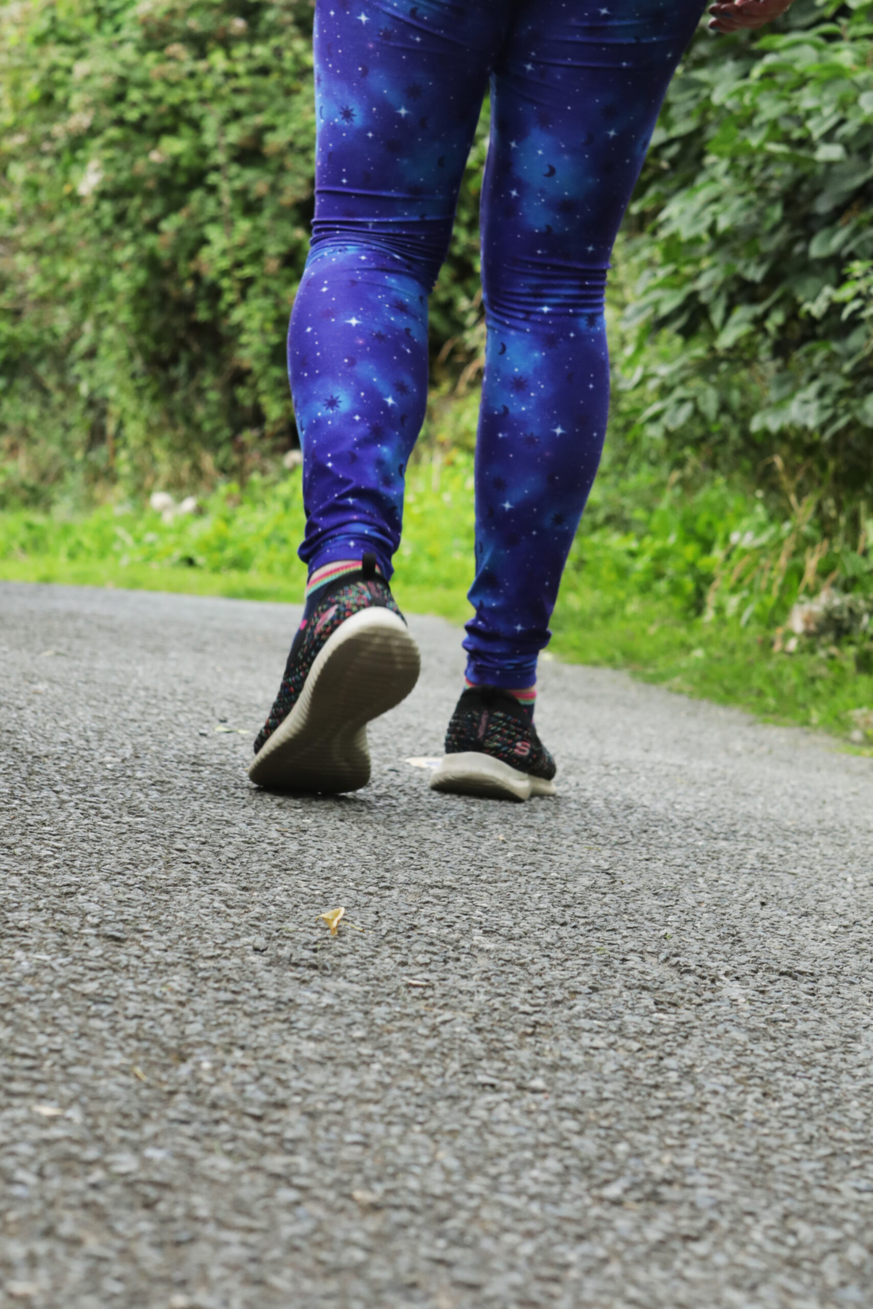 Nant y Pandy Parkrun 11/11/23 1 Jen is walking down a path in her galaxy themed leggings and trainers.