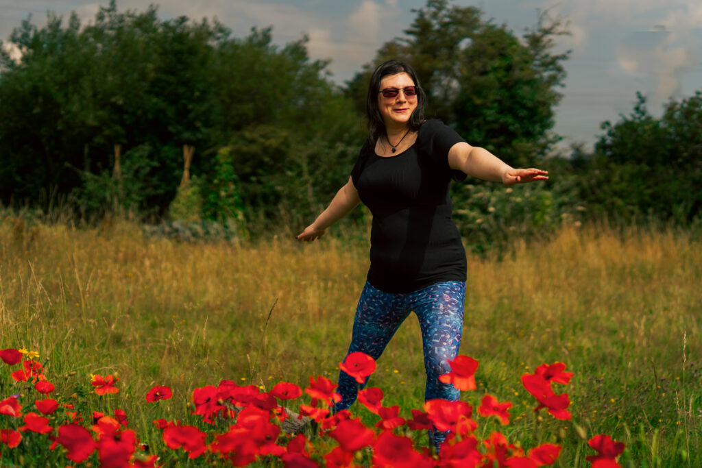 Me doing the warrior pose in a field of poppies for a photoshoot. Wearing sunglasses in my music themed leggings. 