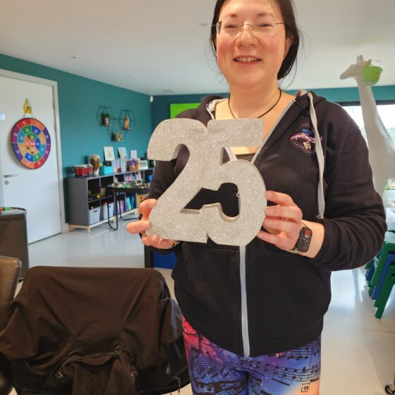 A picture of Jen holding a sparkly 25. Musical leggings, tropic pianist gamer hoodie.