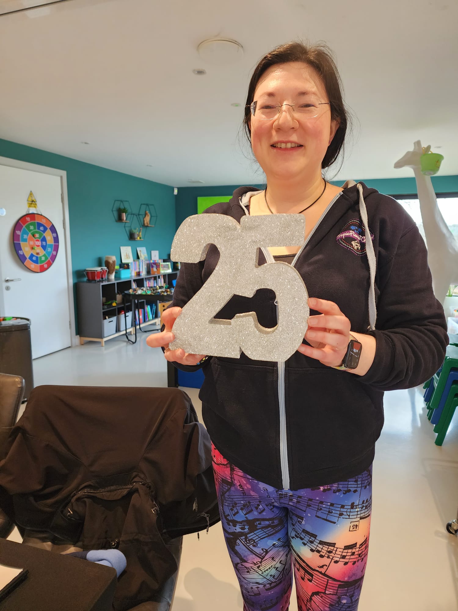 March was an Exciting Month! 1 A picture of Jen holding a sparkly 25. Musical leggings, tropic pianist gamer hoodie.