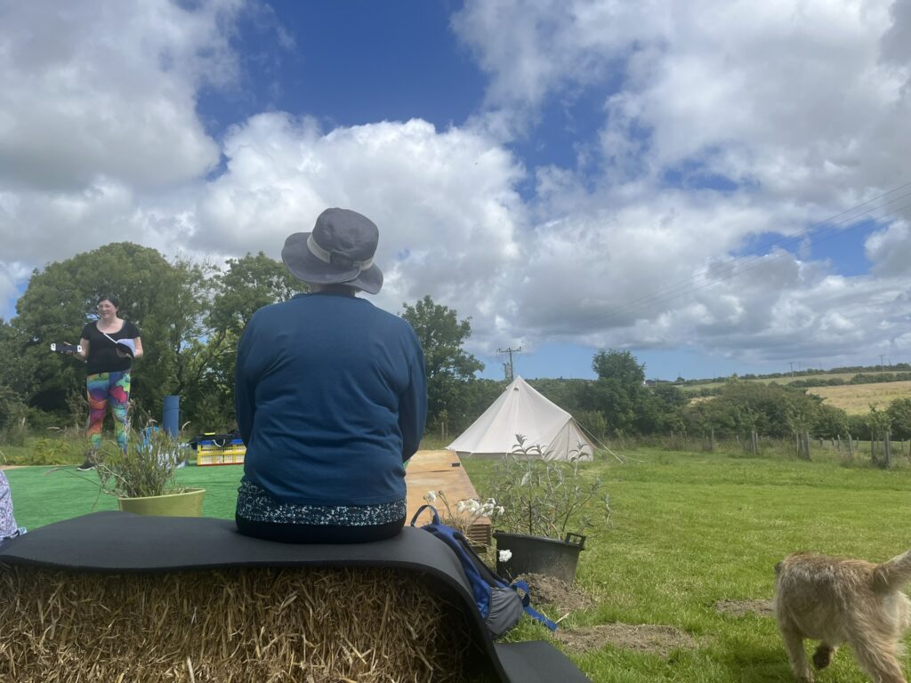 Speaker at a Brand New Yoga Festival- June 2024 - a Major 2024 Goal accomplished! 10 a photo from the audience, of me giving my talk, blue skies above