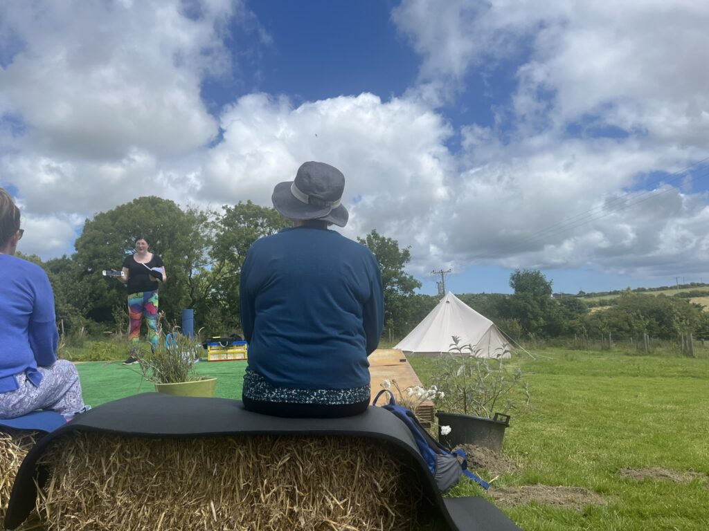 Speaker at a Brand New Yoga Festival- June 2024 - a Major 2024 Goal accomplished! 11 a photo from the audience, of me giving my talk, blue skies above
