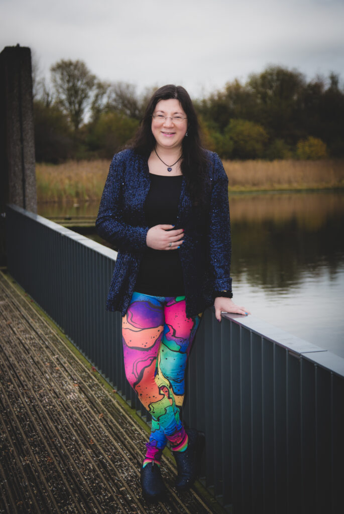 A posed shot in my rainbow leggings, with sparkly navy jacket, leaning on a bridge. 