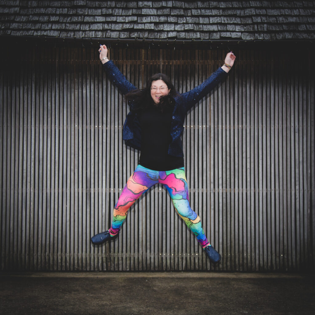 A shot of me star jumping in the air, with rainbow leggings, and navy sparkly jacket.