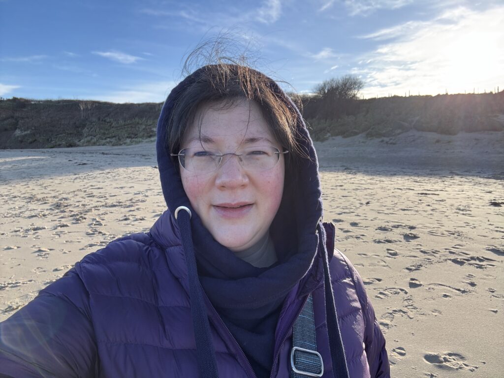2025- New Year, New Chapter! 5 A selfie of Jen freezing on the beach, with hood up.