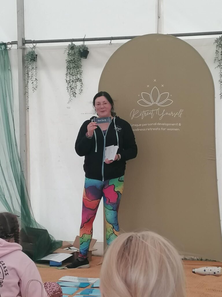 Festivals of 2025 Fulfilled & 3 Public Speaking Goals Smashed! 11 Picture of me holding my book and my bookmark, wearing branded hoodie and rainbow leggings.