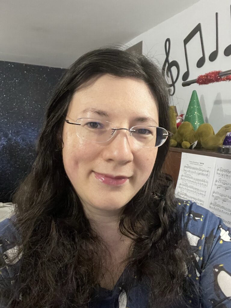 Christmas is looking Different This Year, and I'm Excited for it! 2 A selfie of me by my Festively decorated piano, wearing my Penguin Popsy dress, hair down. Taken in 2021.