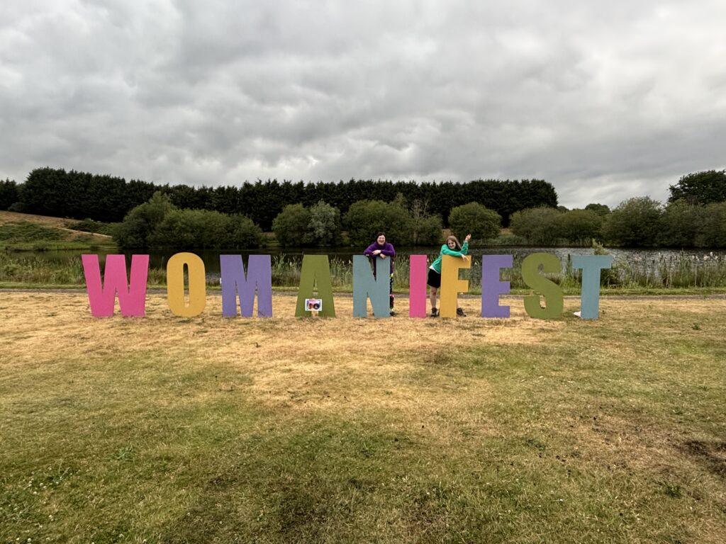 Summer 2026 is a Great Balance! 10 Me and Kirsty stood behind the big Womanifest sign.