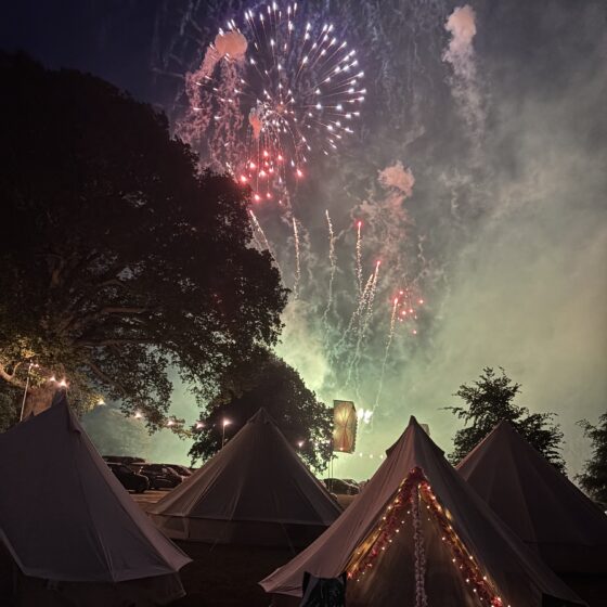 A picture over bell tents at the night sky with a colourful display of fireworks overhead.