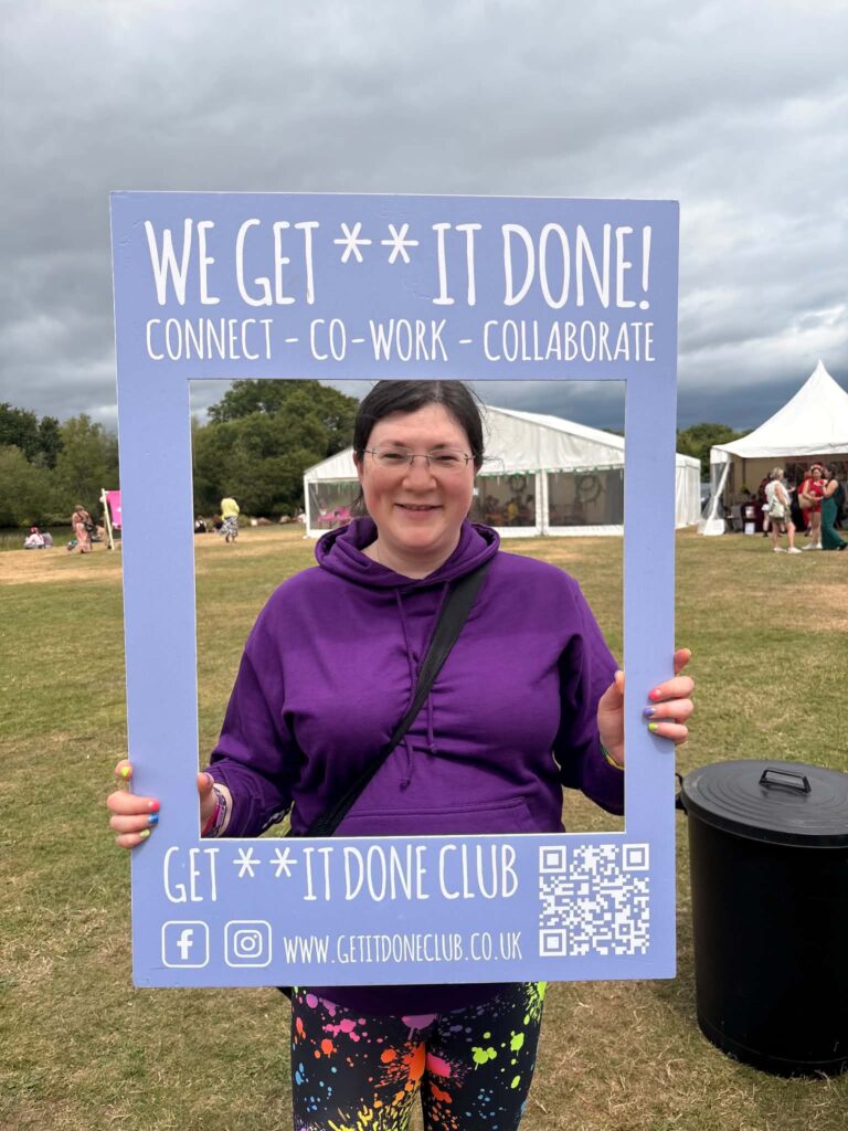 Summer 2026 is a Great Balance! 7 A picture of me standing with the Get it Done club selfie frame, smiling, with violet hoodie.